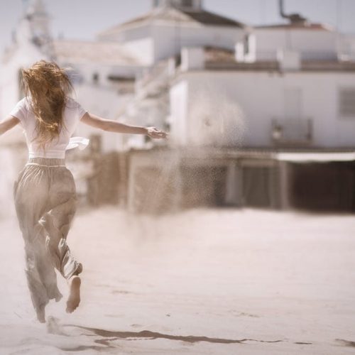 Back view of a young woman jumping and enjoying on a sunny beach, embodying freedom and happiness.