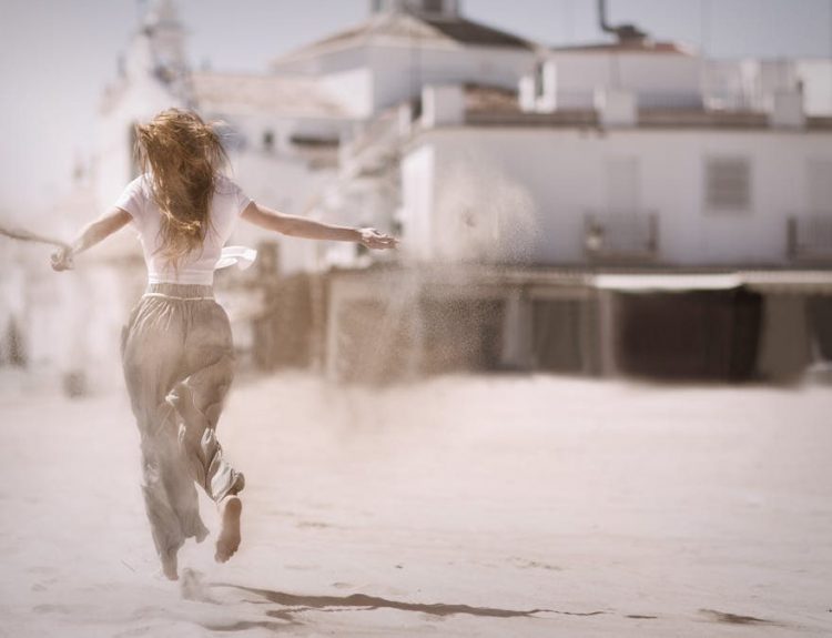 Back view of a young woman jumping and enjoying on a sunny beach, embodying freedom and happiness.