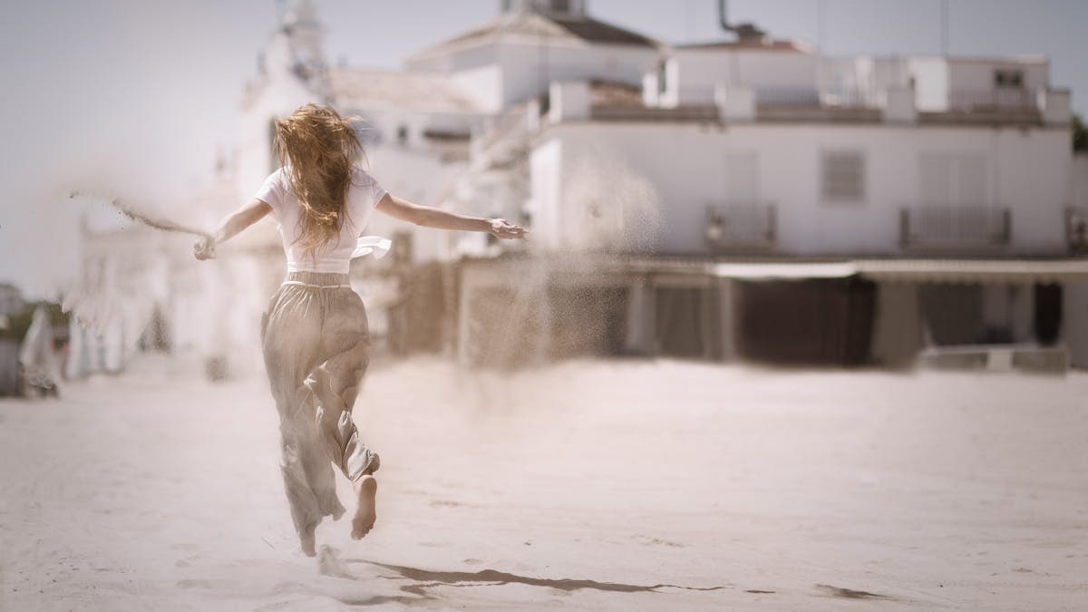 Back view of a young woman jumping and enjoying on a sunny beach, embodying freedom and happiness.